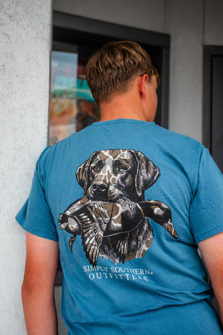 A man viewed from behind wearing a blue t-shirt with a large graphic of a black and white dog holding a duck, with the text 'SIMPLY SOUTHERN OUTFITTERS' printed below.