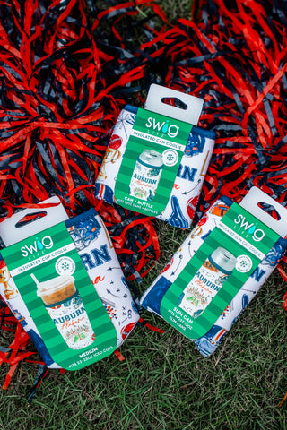 Three SWG Mini Pitcher Bags with Australian-themed designs are arranged on green grass amidst red and black tinsel. The bags feature patterns of kangaroo kangaroo's feet, the word 'AUSTRALIA,' and a green-and-white striped banner.