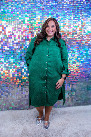 A woman modeling a green long-sleeve button-up shirt dress with subtle white speckles, standing on a white shag rug in front of a colorful holographic mirror backdrop.